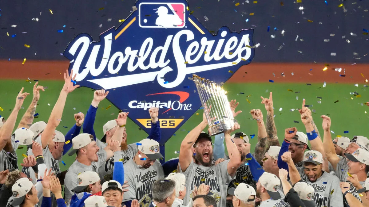 Baseball players celebrate beneath a World Series sign while confetti falls and a trophy is raised.