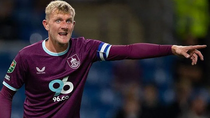 Footballer in a purple Burnley jersey points across the pitch during a match