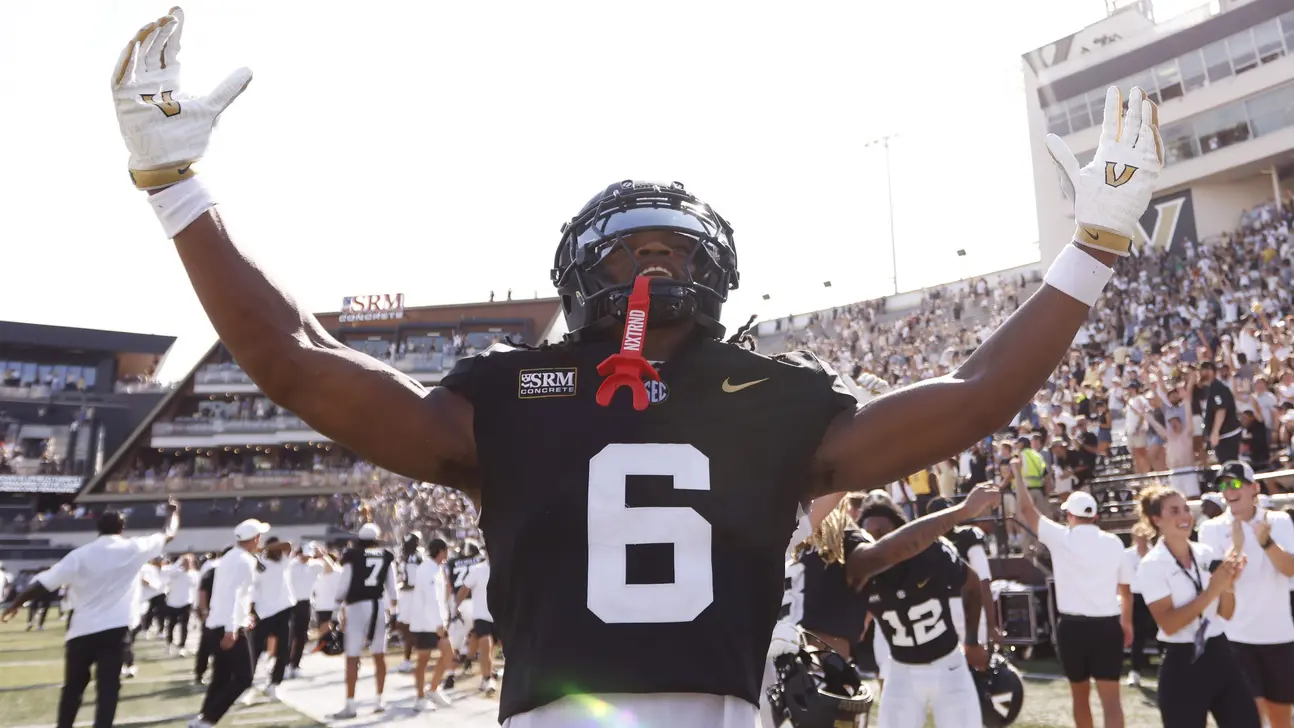 Football player wearing number 6 raises both arms as teammates and fans celebrate behind him