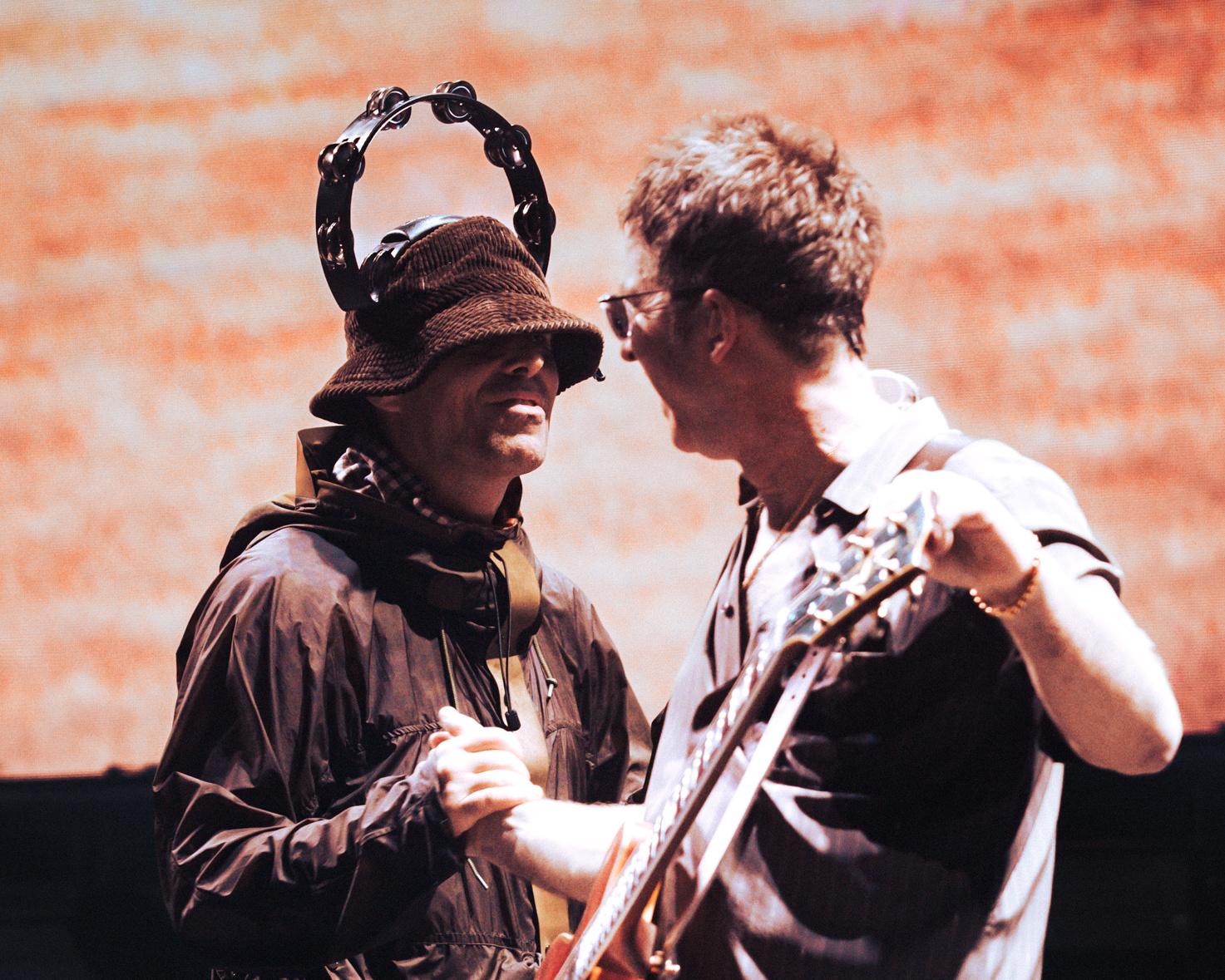 Two musicians face each other onstage, one holding a tambourine and the other playing guitar.