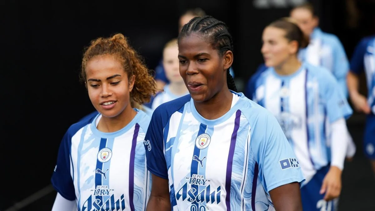 Two Manchester City women players walk together in blue-and-white shirts ahead of a match.
