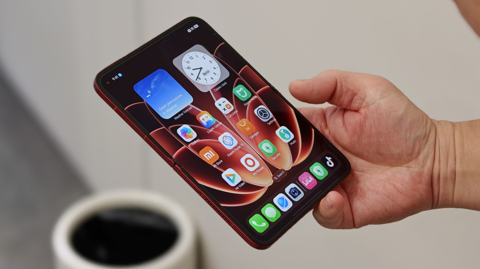 Hand holding an open red foldable smartphone displaying a colorful app-filled home screen