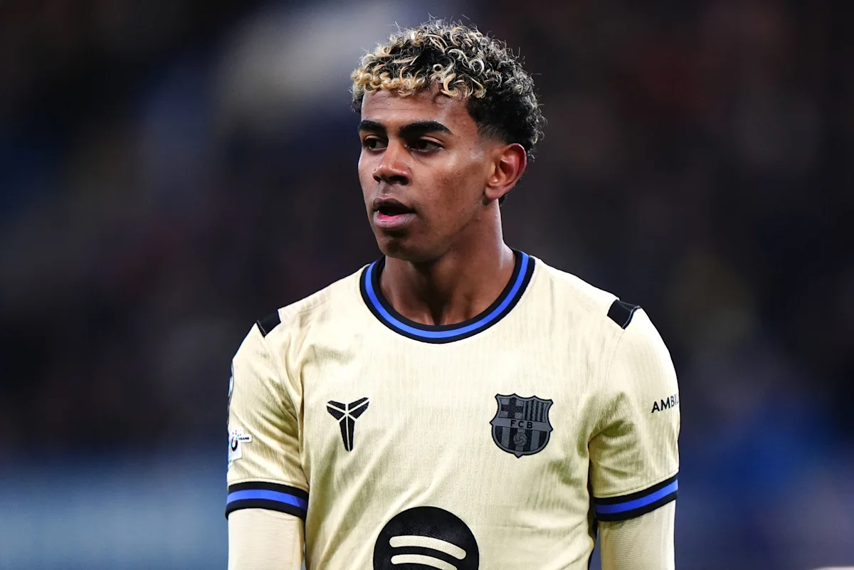 Barcelona footballer in cream jersey with blue trim stands against a blurred stadium background