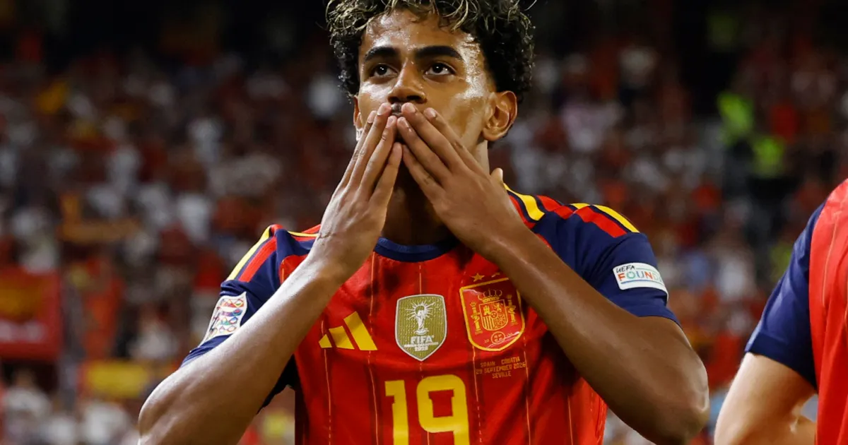 Spain player in a red number 19 shirt blows a kiss toward the crowd.