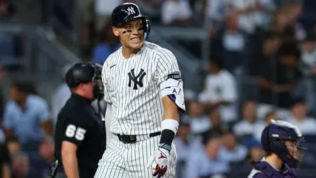 Yankees player in pinstripes stands near home plate with an umpire and catcher nearby