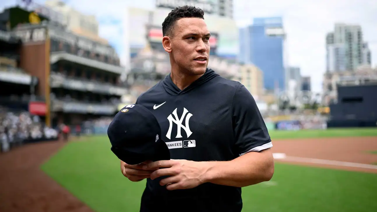 Man in Yankees jersey holding a baseball cap on a baseball field