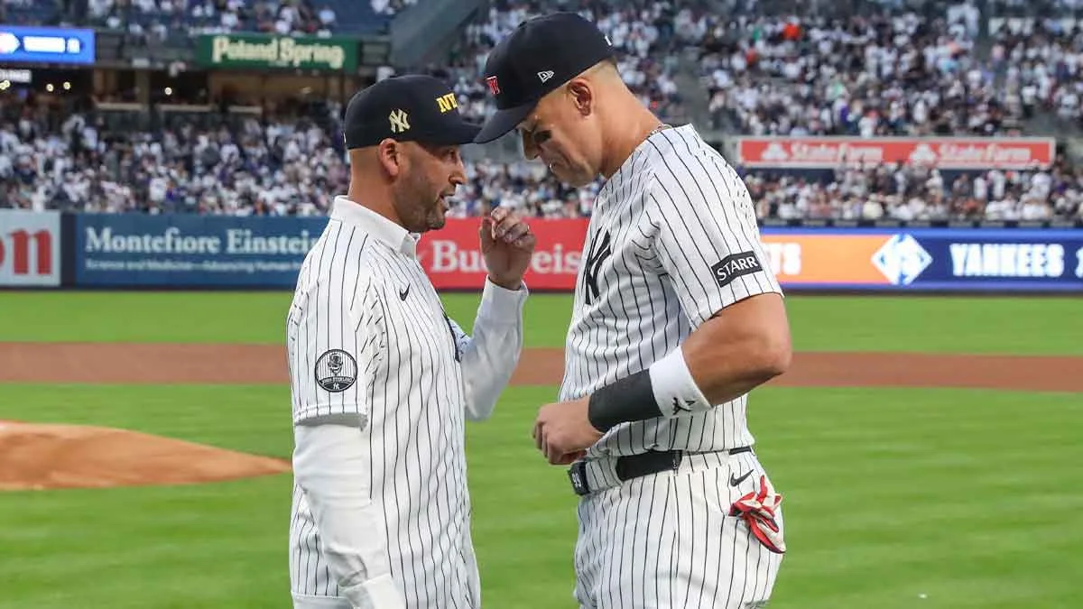 Two Yankees players in pinstriped uniforms converse on the field near the pitcher's mound.