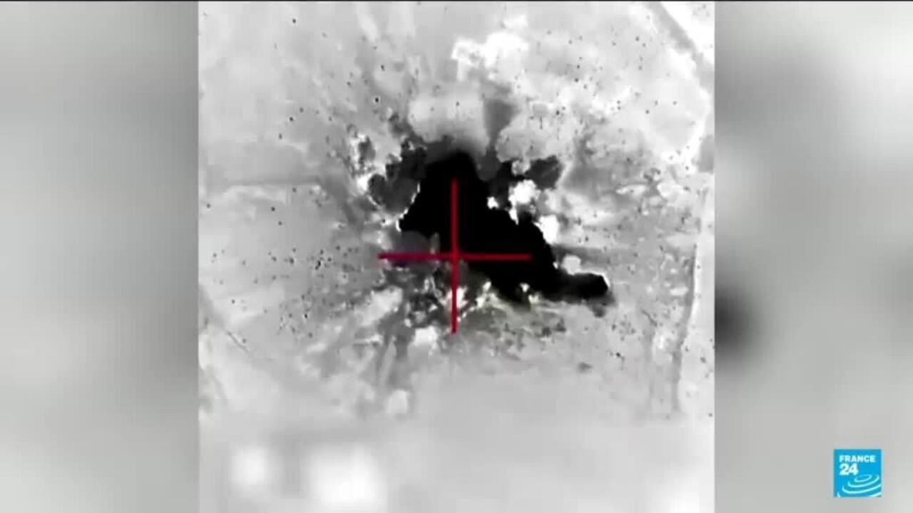Monochrome aerial imagery shows a dark central area marked by a red targeting crosshair.