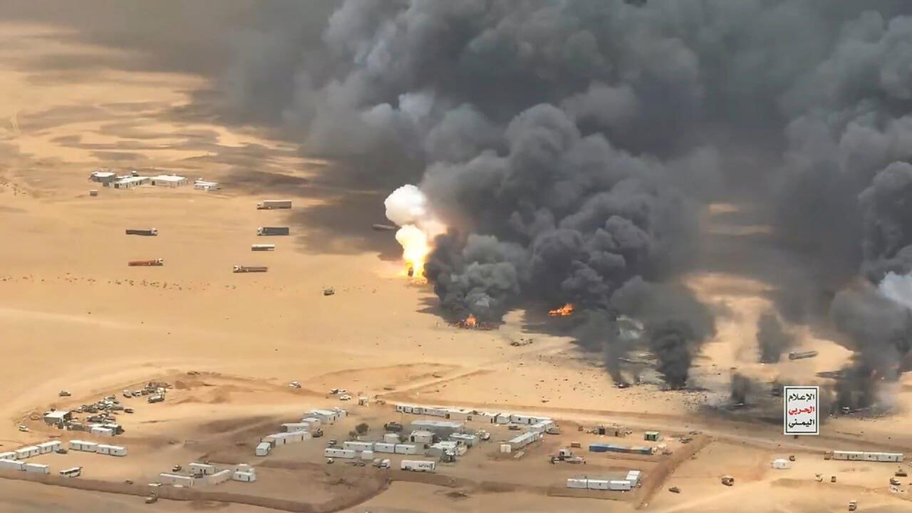 Aerial view of fires and thick black smoke rising beside a desert encampment.