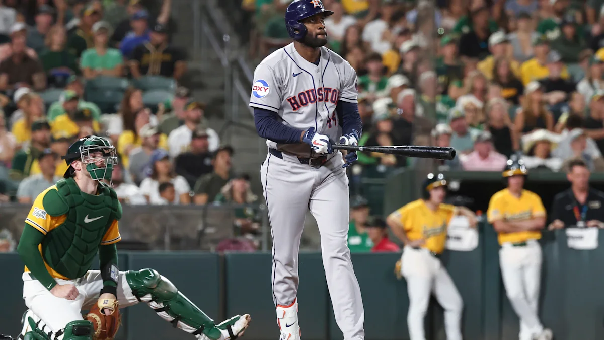 Astros batter stands at home plate as an Athletics catcher crouches and fans watch.