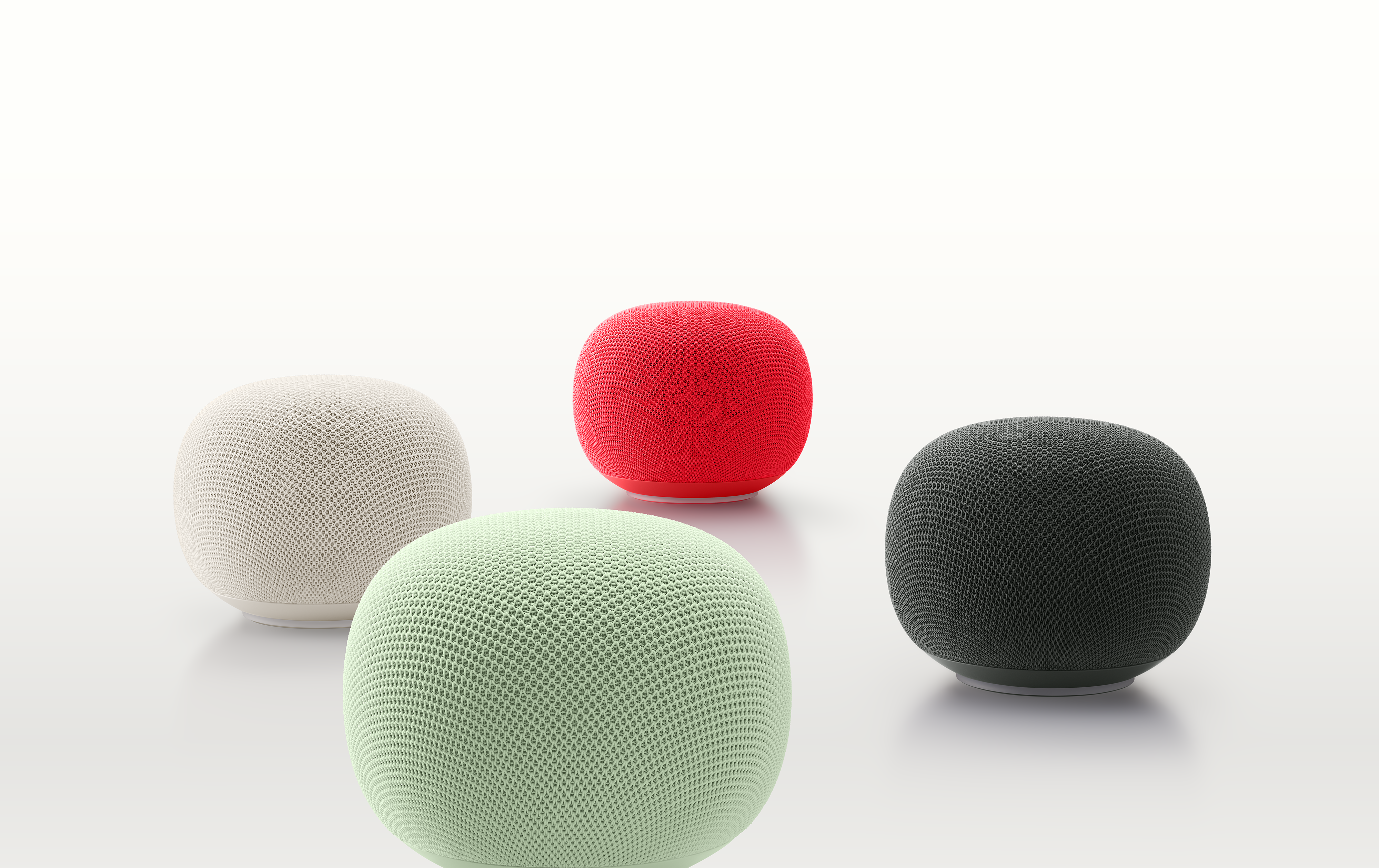Four fabric-covered smart speakers in white, red, green, and black arranged on a light surface.