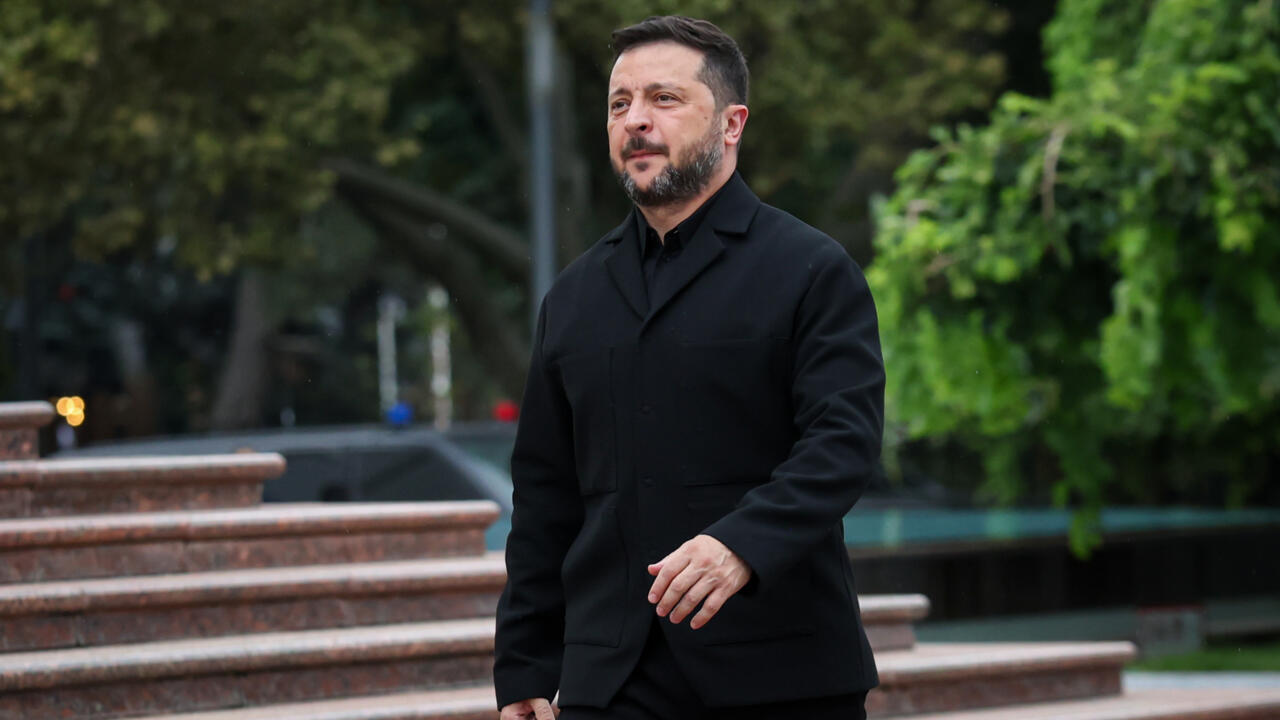 Man in black coat standing outdoors near stone steps and trees