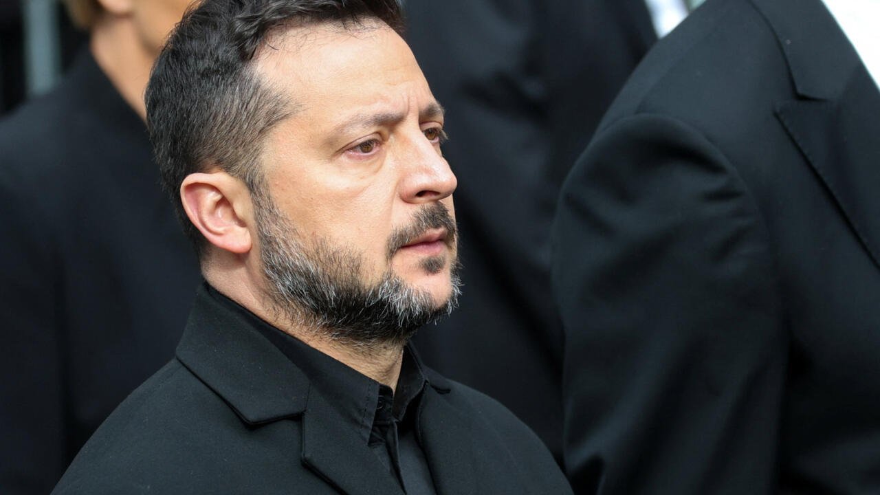 Bearded man in black coat looks to the side among people wearing dark clothing