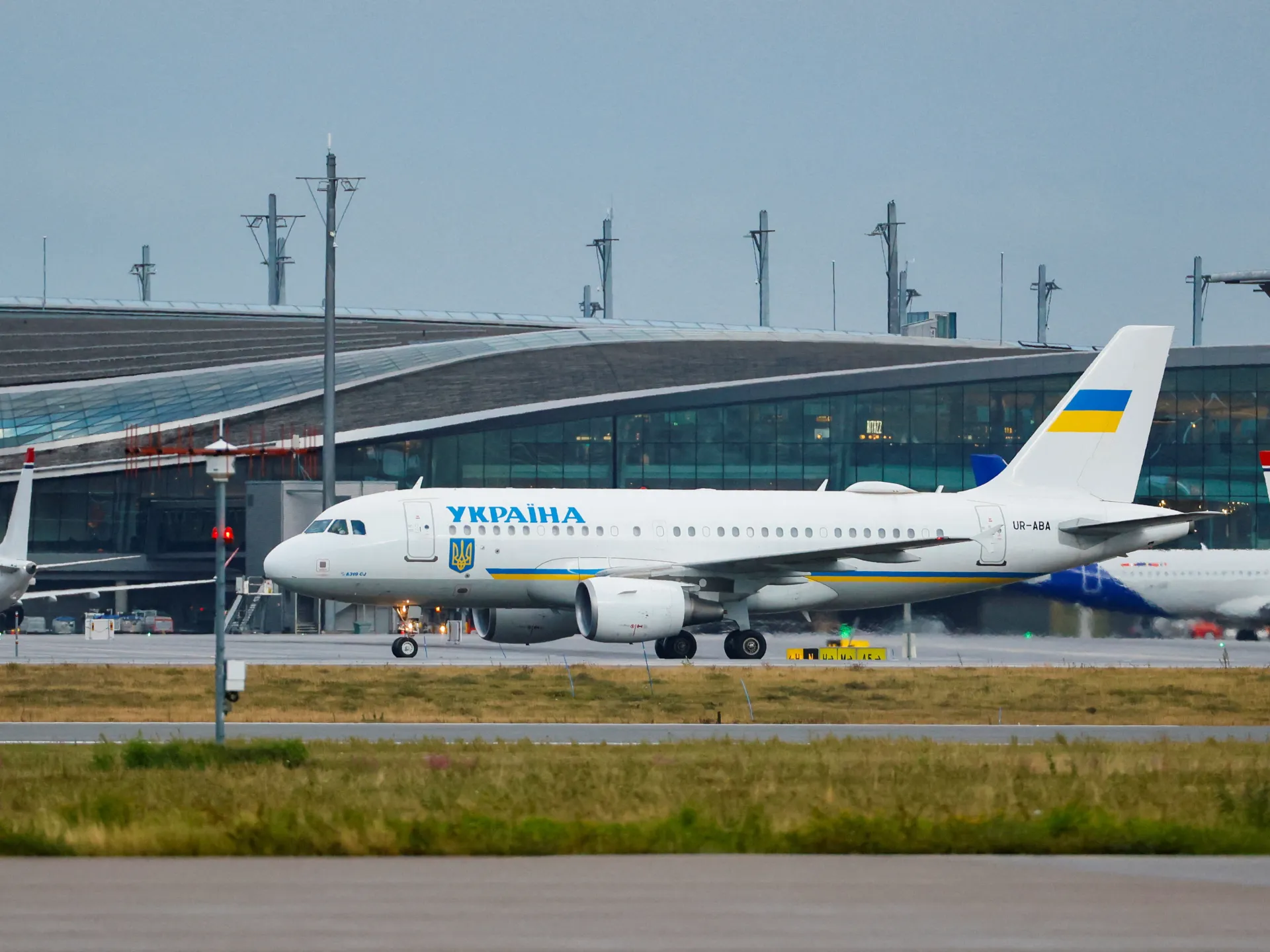 Ukrainian government airplane taxiing past an airport terminal with another aircraft behind it.