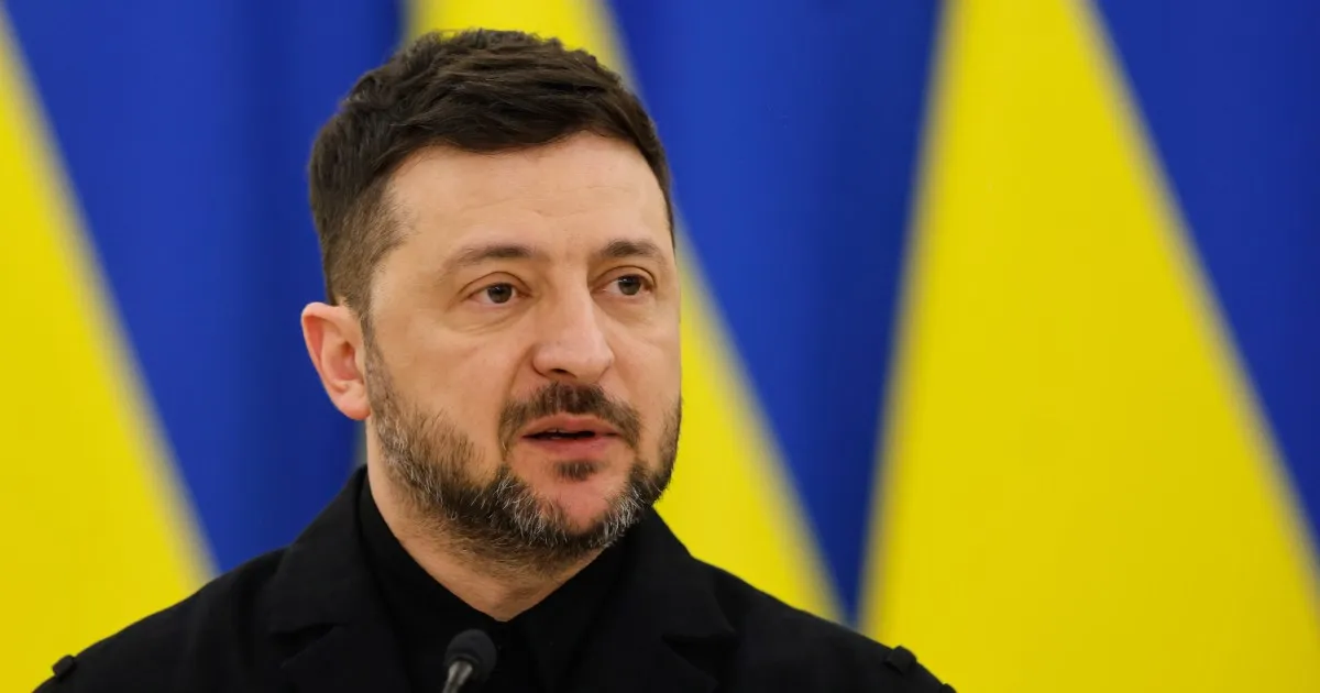 Ukrainian President Volodymyr Zelenskyy speaking before a blue-and-yellow Ukrainian flag