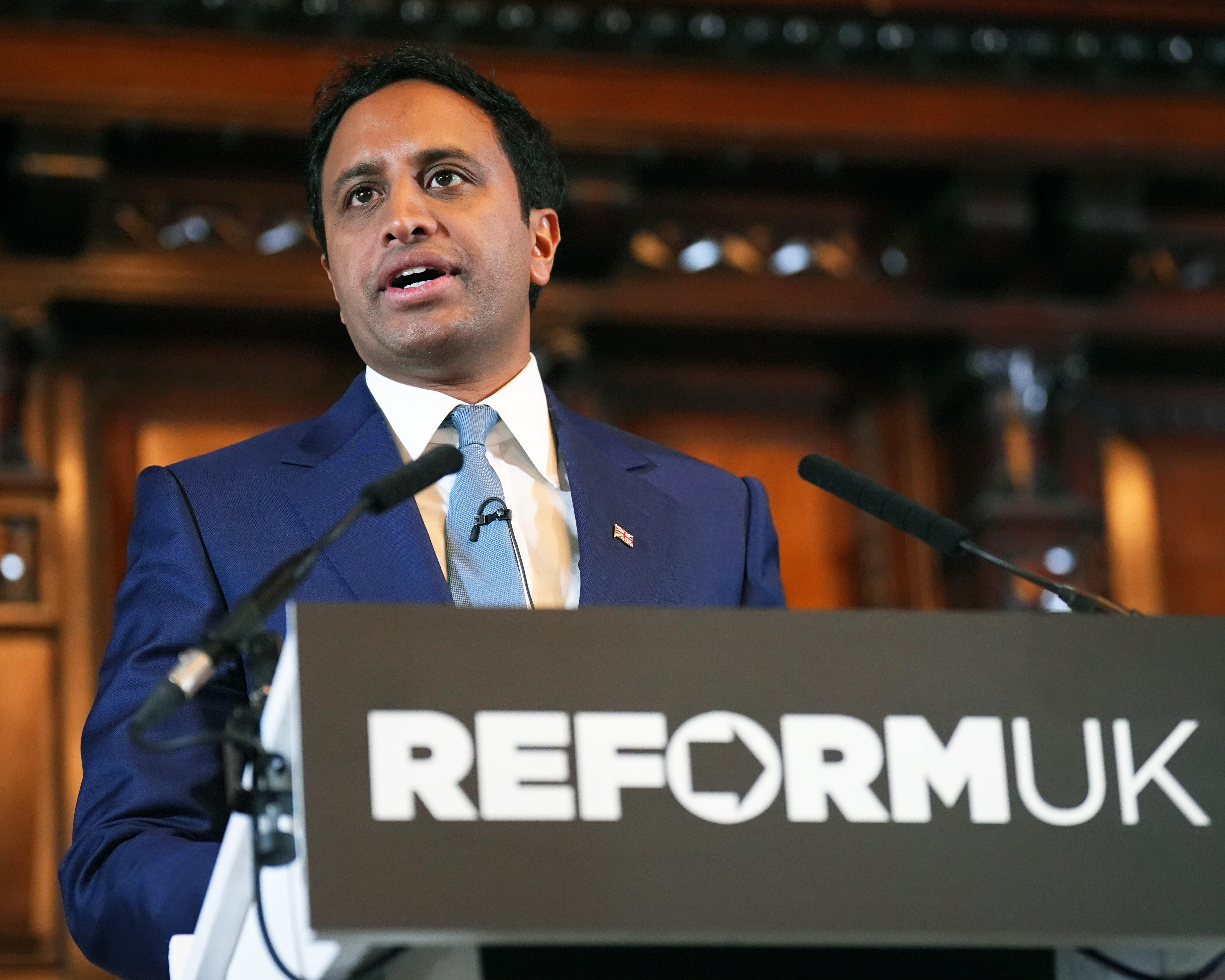 Man in blue suit speaking at a podium with microphones in a formal interior