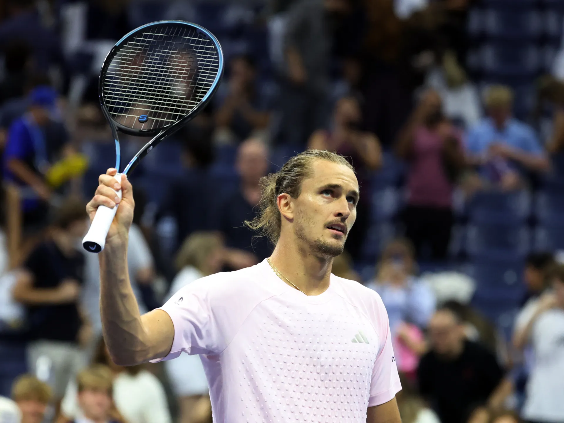 Tennis player in pink shirt raises a racket before a blurred spectators' crowd