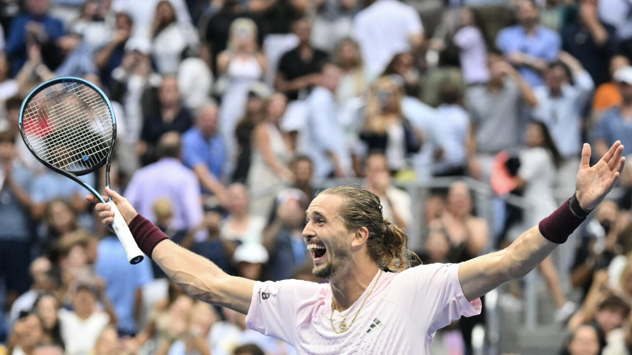 Tennis player celebrates with arms outstretched while holding a racket before a blurred crowd