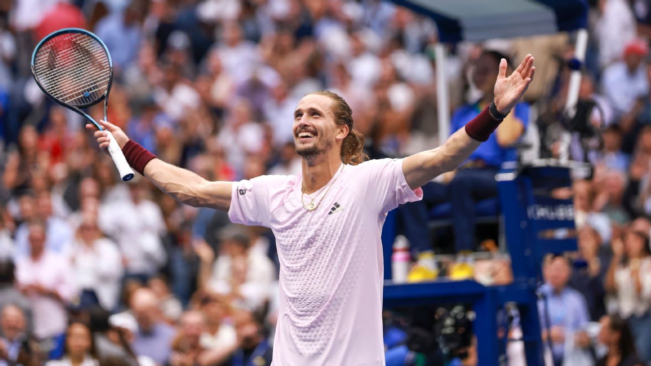 Tennis player celebrates with arms outstretched while holding a racket before a blurred crowd.