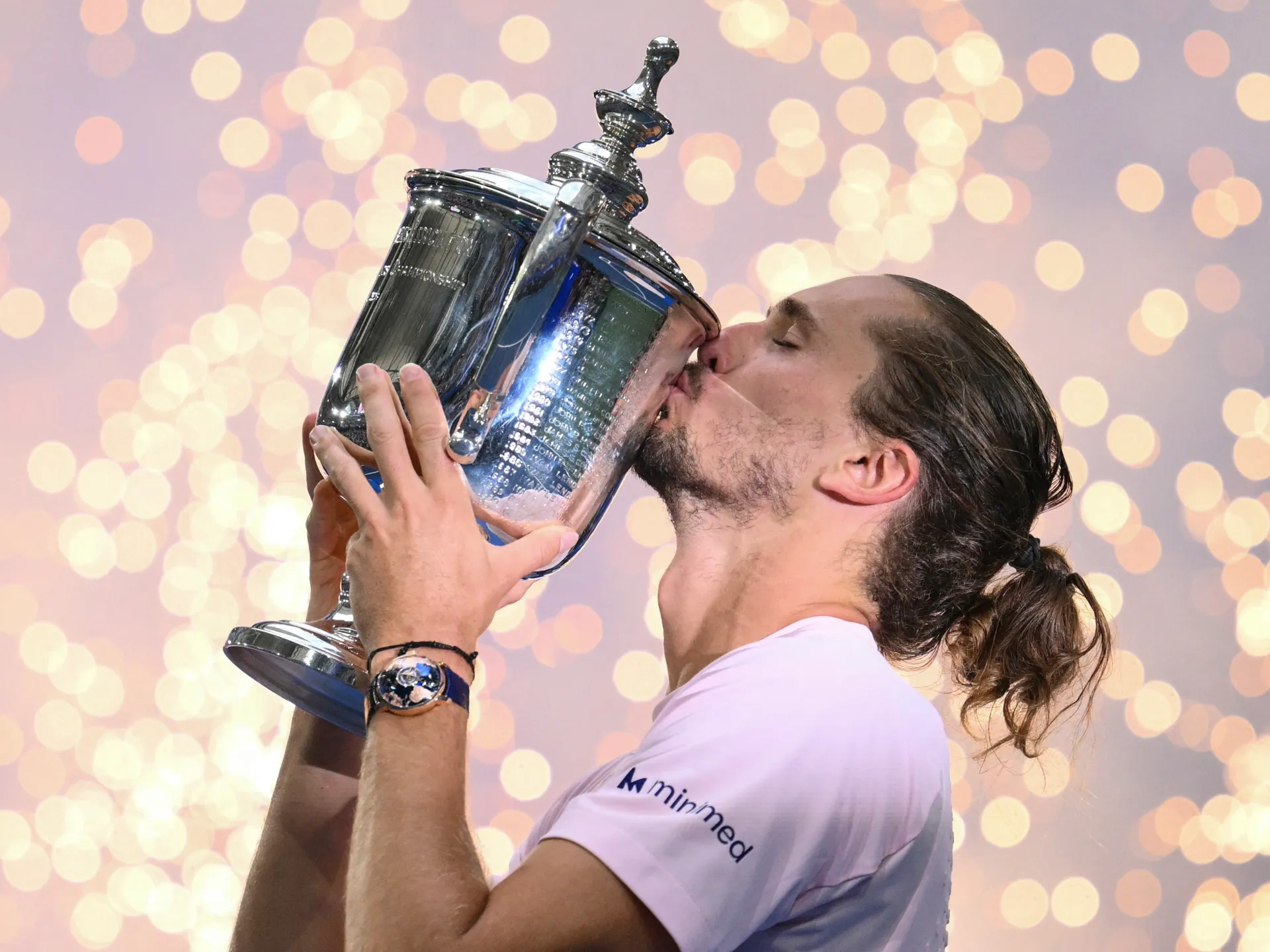 Tennis player kisses a large silver trophy amid softly blurred celebratory lights
