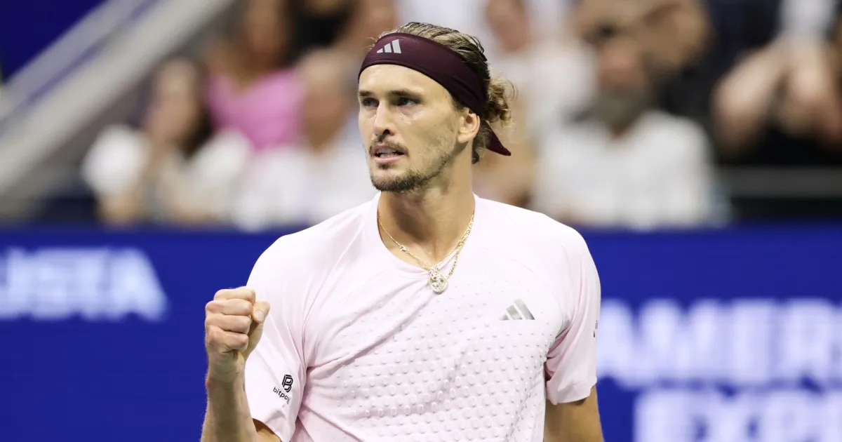 Tennis player in a pale pink shirt and maroon headband raises a clenched fist.