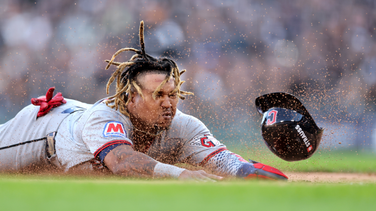 A baseball player slides headfirst through dirt as his helmet flies off nearby.
