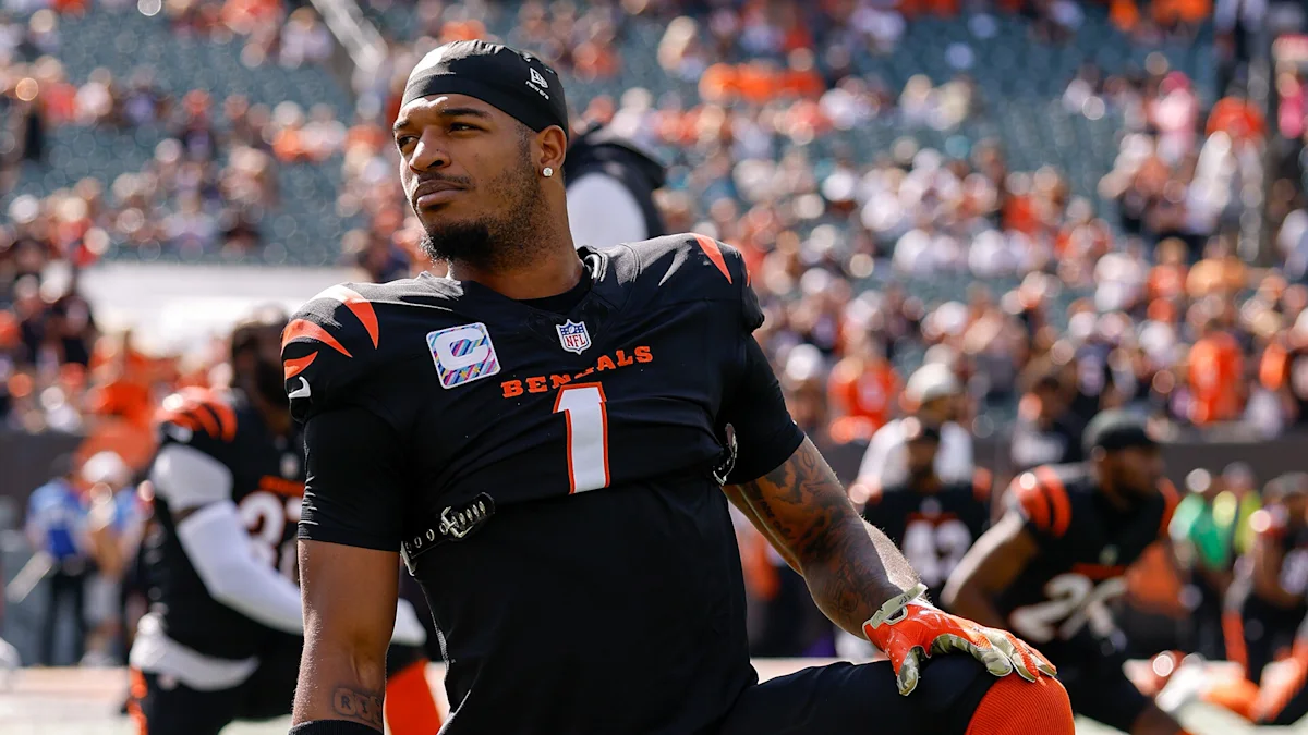 Football player in a black number 1 jersey and orange gloves stands on the field amid a blurred crowd.