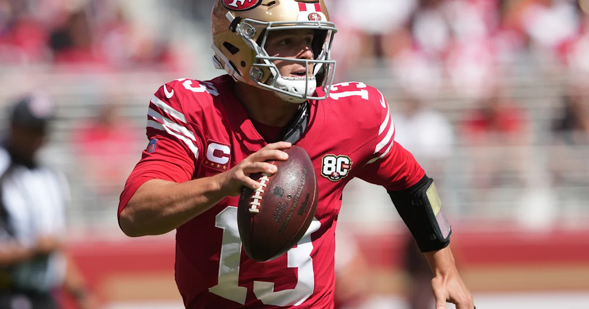 San Francisco 49ers player in a red uniform runs with the football during a game.