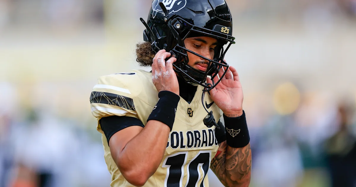 Colorado football player in a black helmet adjusts his chin strap during a game.