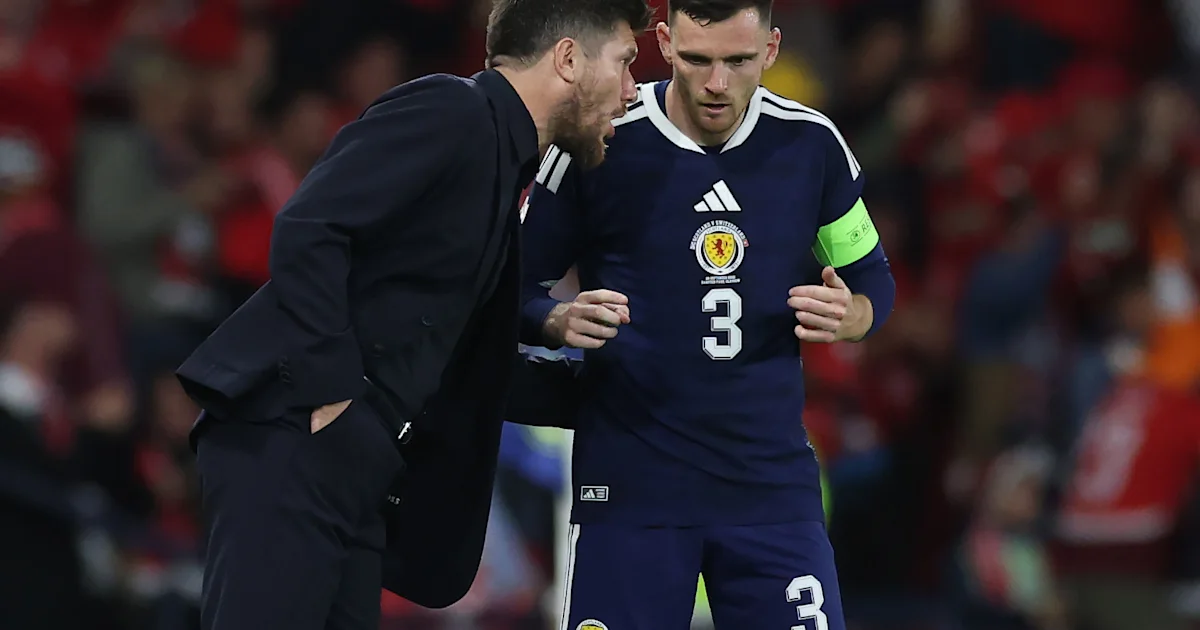 A suited man leans toward Scotland captain Andrew Robertson in a navy kit and green armband.