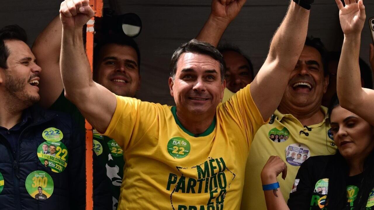 A man in a yellow shirt raises both arms amid a crowd wearing political campaign badges.