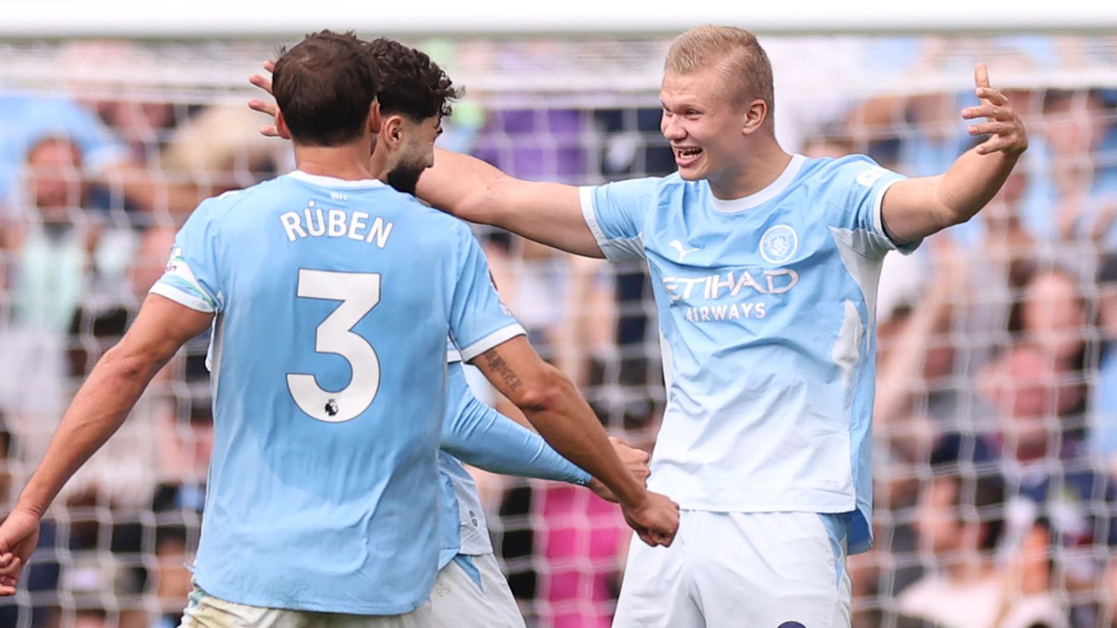 Manchester City players in sky blue shirts celebrate together, with one player raising both arms.
