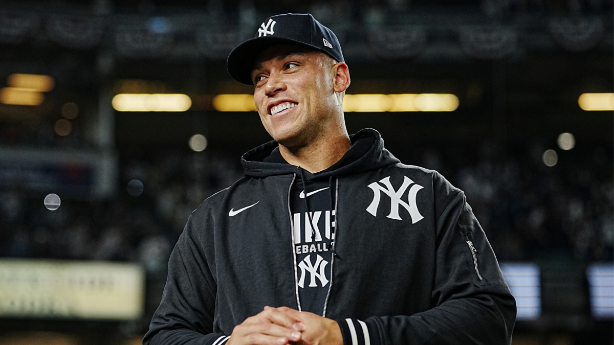 Smiling man in a Yankees cap and black team jacket stands inside a baseball stadium.