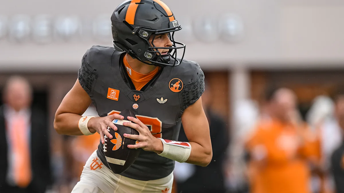 Tennessee quarterback in a dark uniform holds the football and looks to his right.