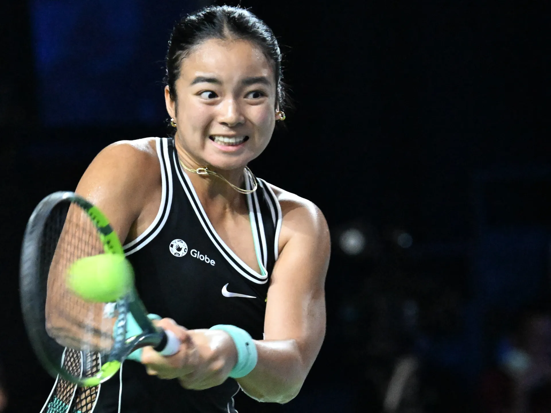 Tennis player in a black and white top swings at a neon green ball.