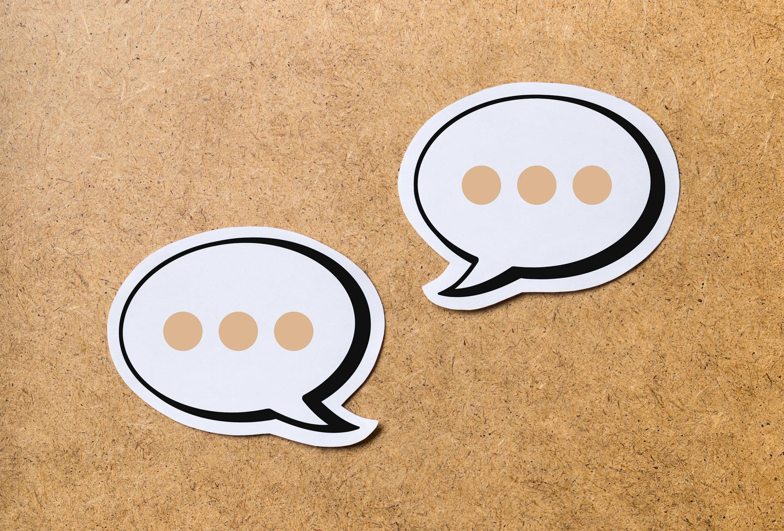 Two overlapping white speech bubble cutouts with black outlines and beige ellipses on a corkboard.