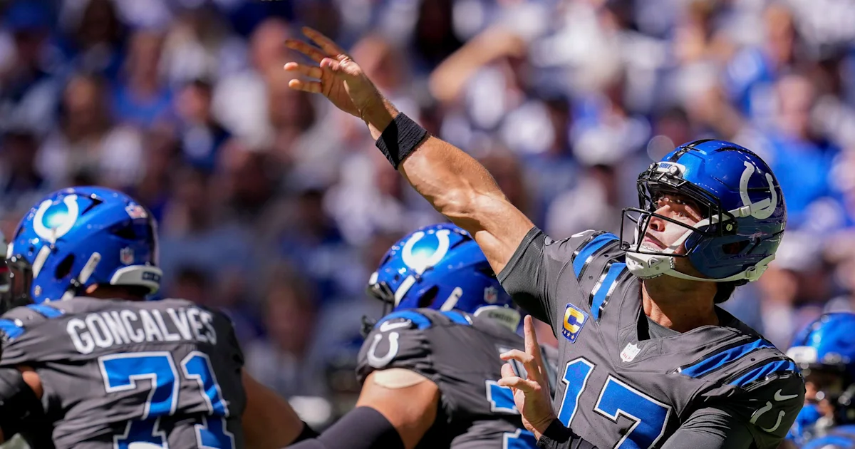 Colts quarterback in a blue helmet raises his throwing arm behind two teammates on the field.