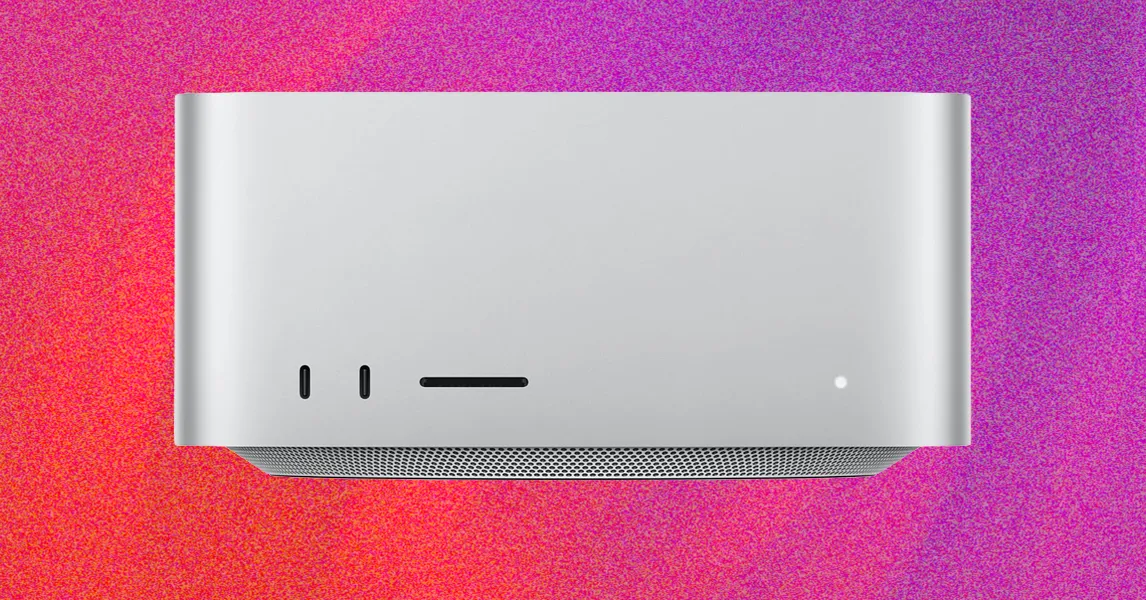 Silver desktop computer with front ports and indicator light against a vivid pink and purple background.
