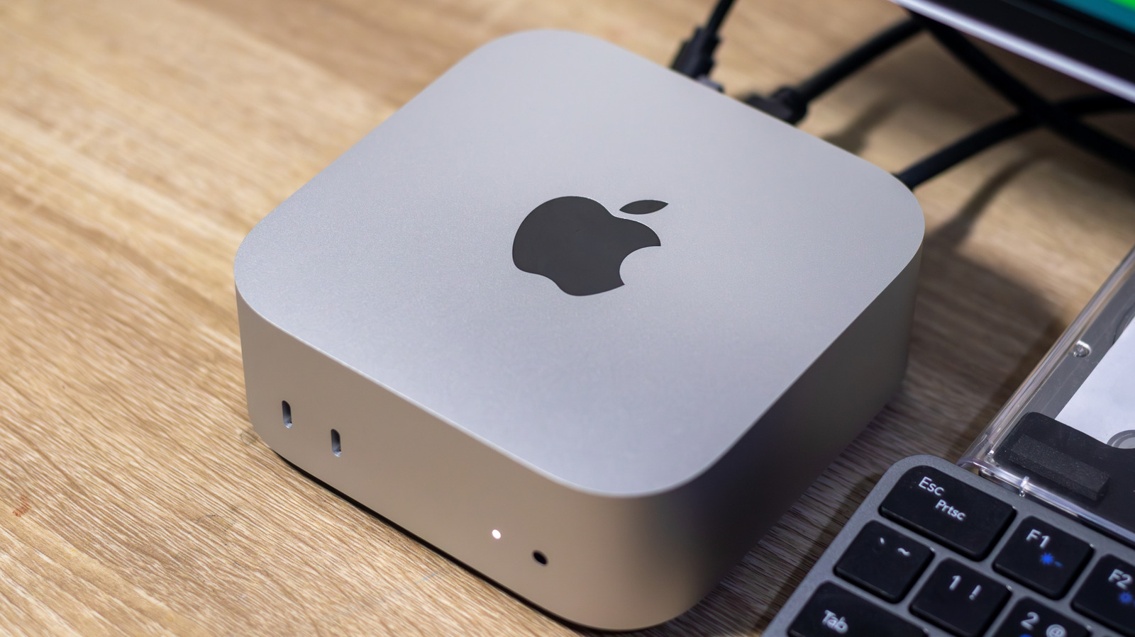 Silver Apple desktop computer with a black logo on a wooden desk beside a keyboard.