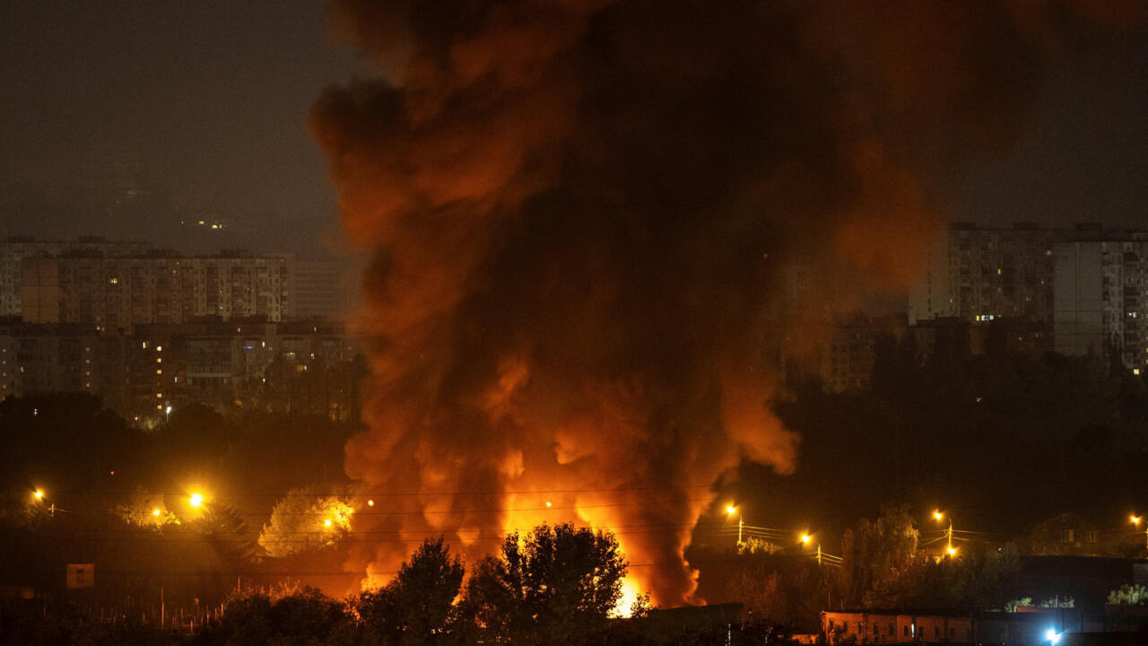 A large plume of smoke and flames rises near apartment buildings at night.