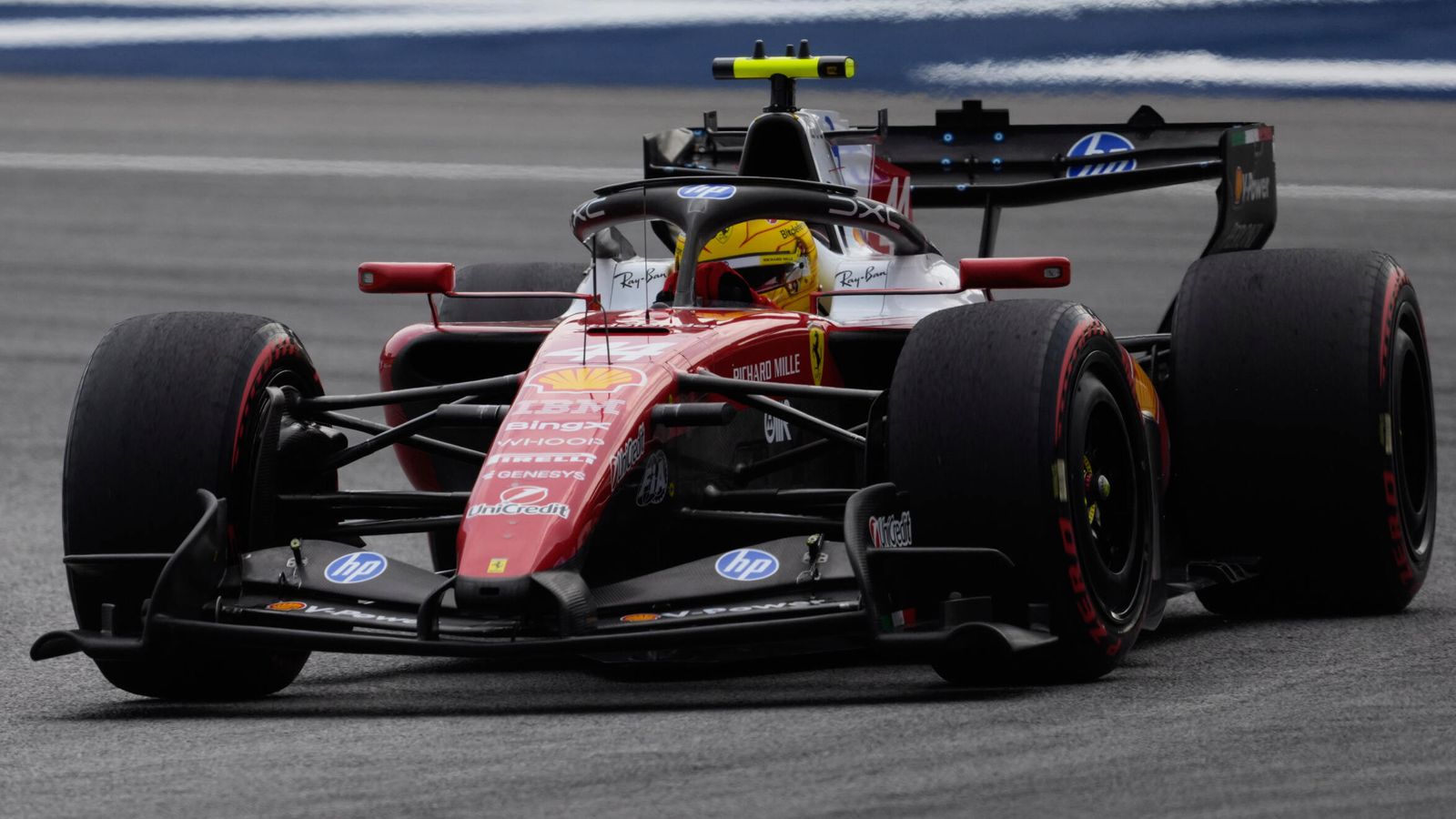 Red Formula One car with a helmeted driver on a wet-looking track, viewed from the front.