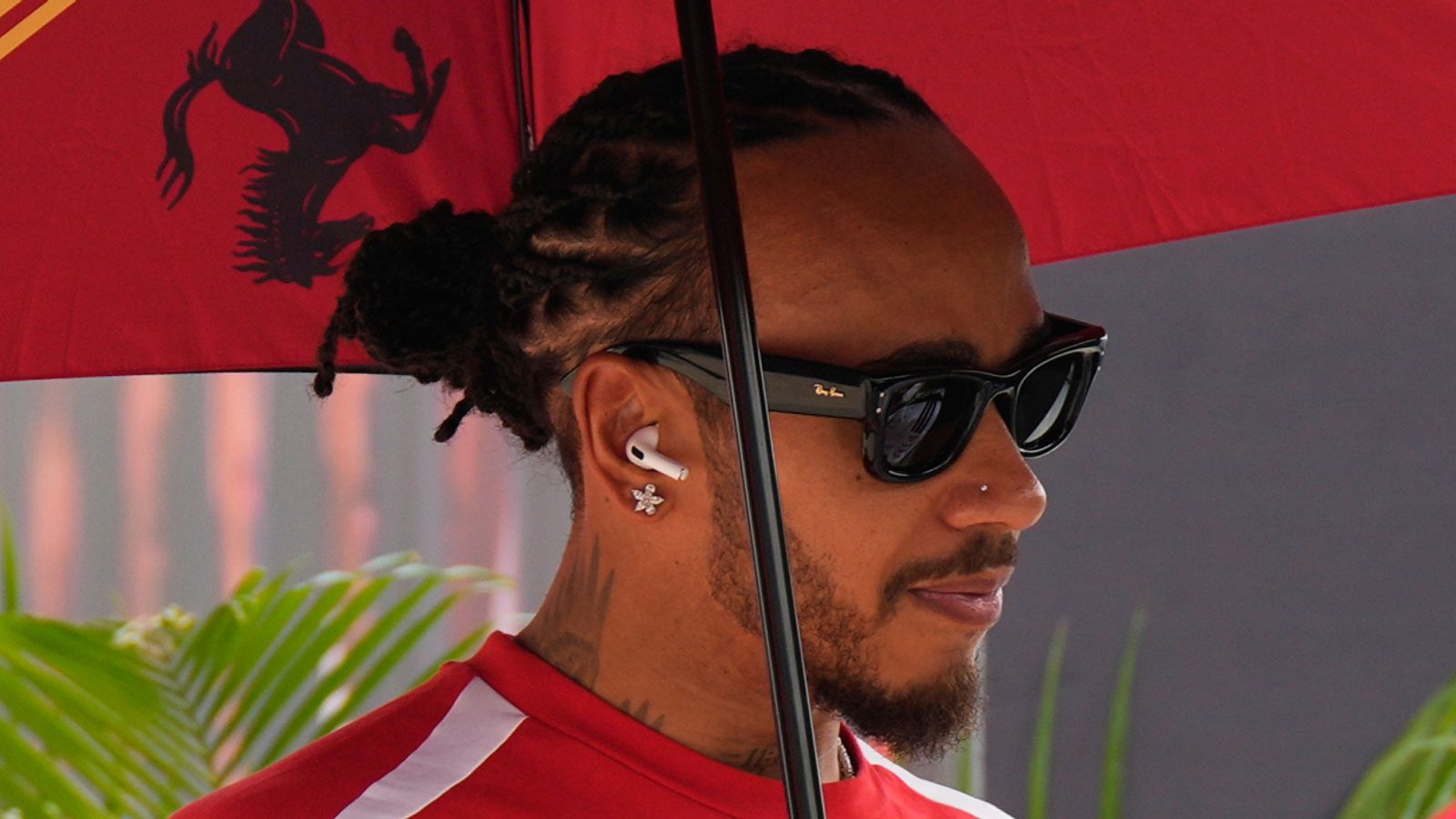 A man in sunglasses and a red-and-white shirt stands beneath a red umbrella.