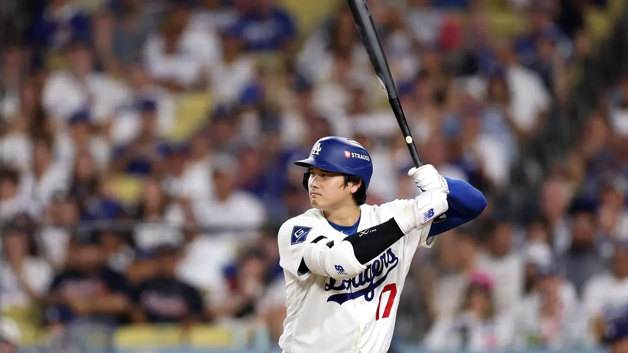 A Dodgers batter in a white uniform and blue helmet holds his bat upright during a game.