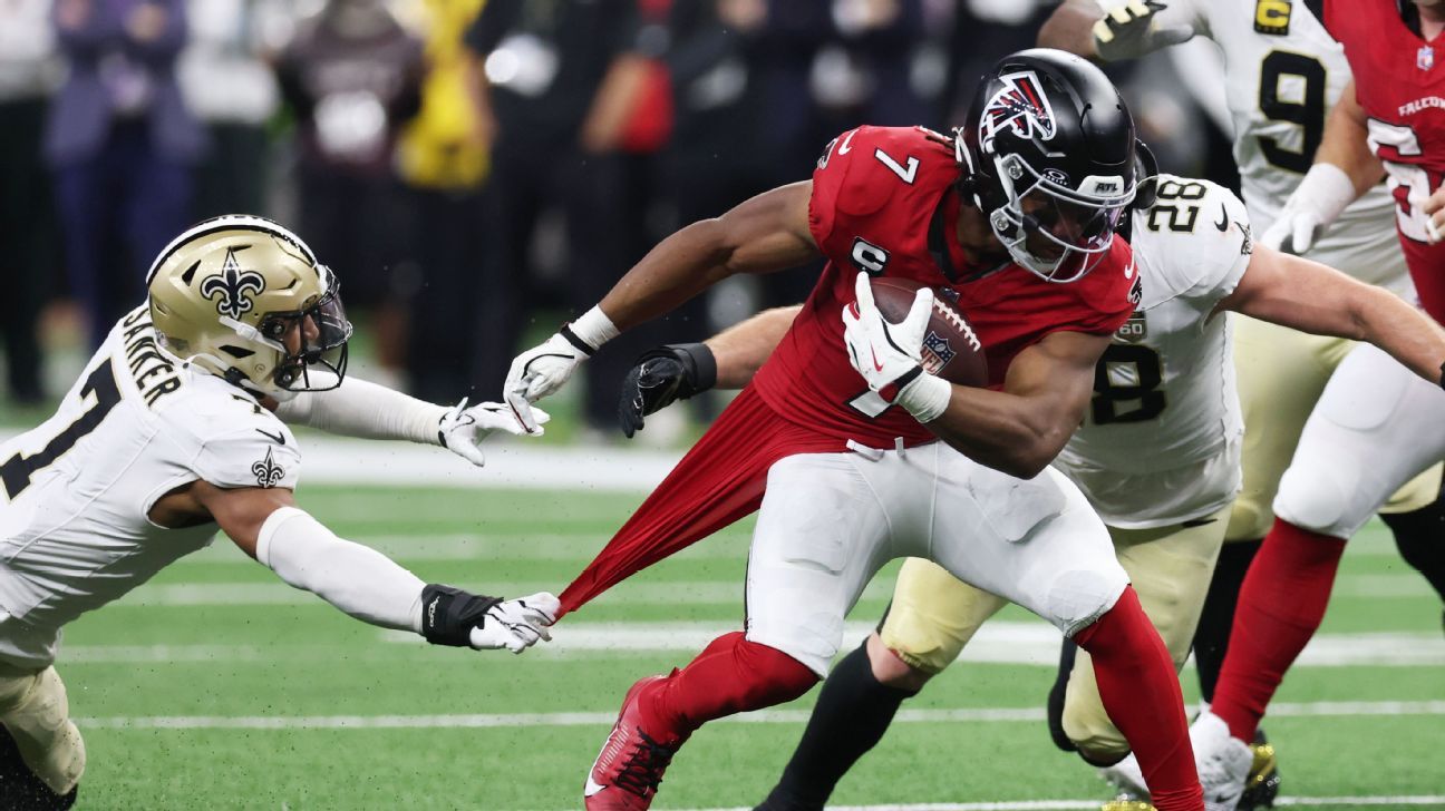 A Falcons player in red runs with the ball as a Saints defender grabs his jersey.