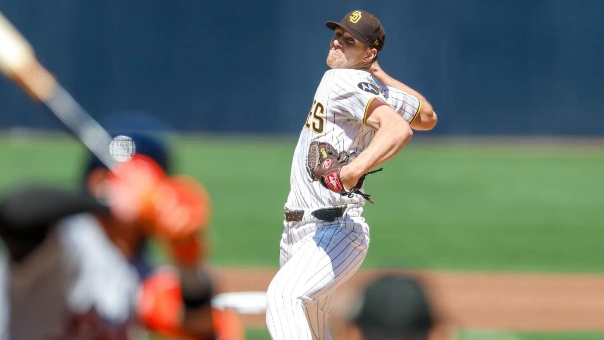 Padres pitcher in a white pinstriped uniform winds up as a blurred batter waits at the plate.