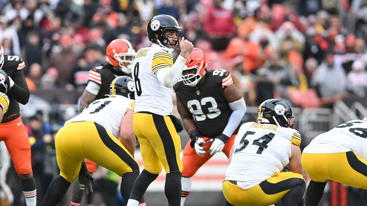 Steelers quarterback prepares to throw as Browns defenders close in during a football game.
