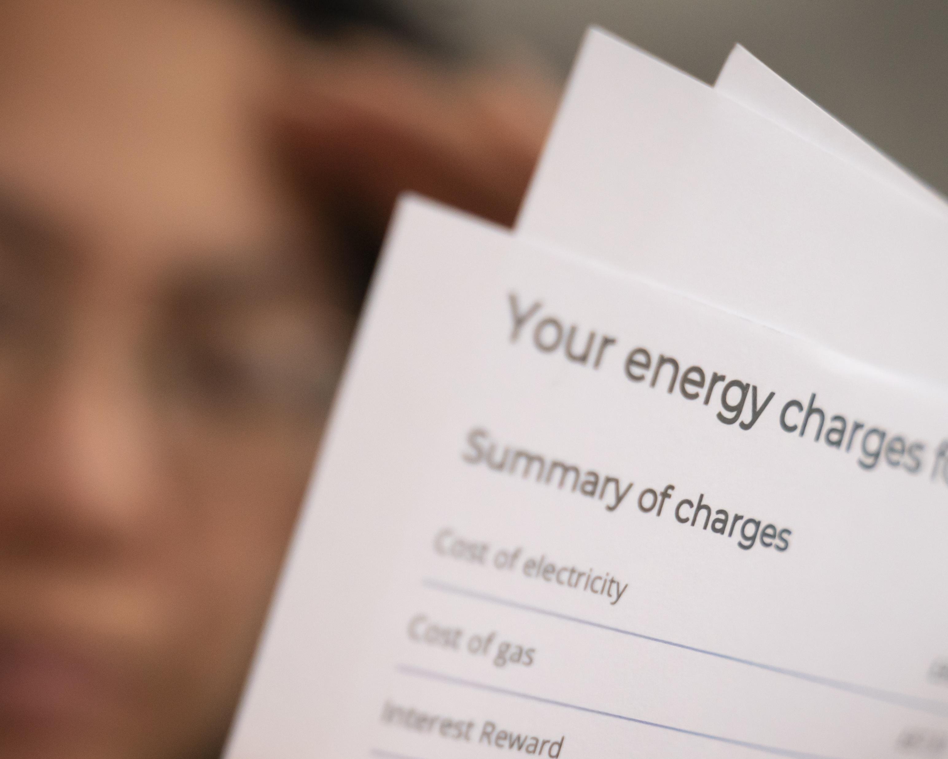 Close-up of an energy bill showing a summary of charges, with other papers behind it.