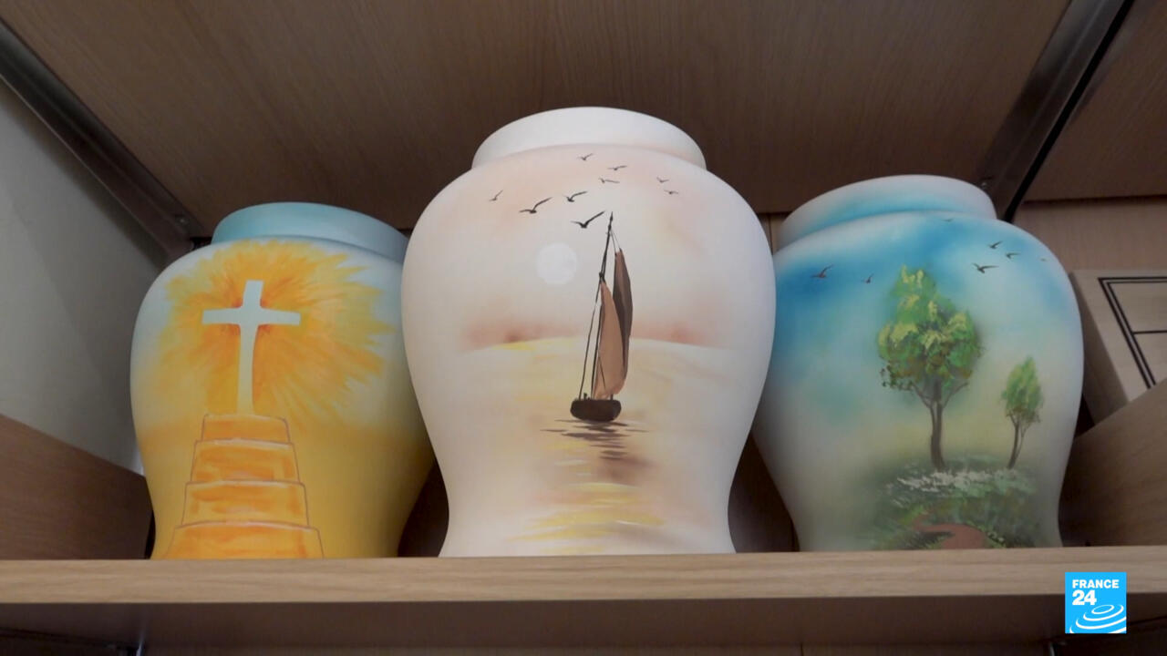 Three painted urns on a shelf depict a cross, a sailboat, and trees.