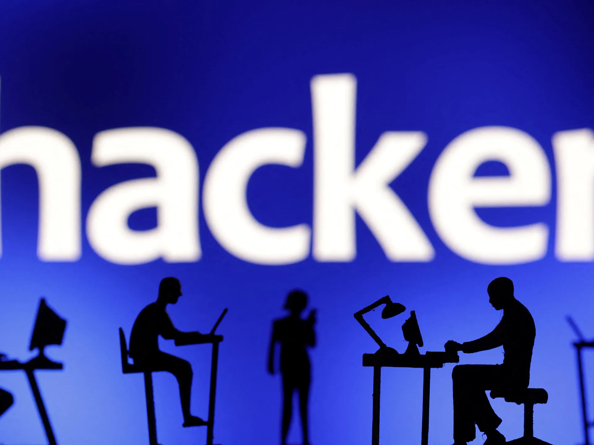 Silhouettes of people working at computers beneath large, cropped white lettering on a blue background.