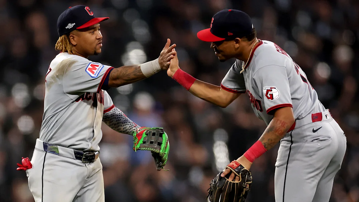 Two Cleveland players in gray uniforms high-five during a baseball game, one holding a green glove.